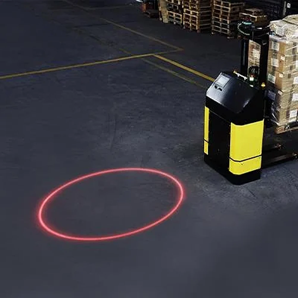 Red laser circle on a warehouse floor beside a mobile robot