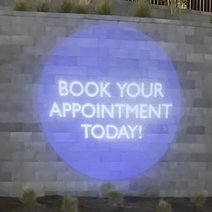 Book Your Appointment Today projected on The Aire's stone entrance wall at night