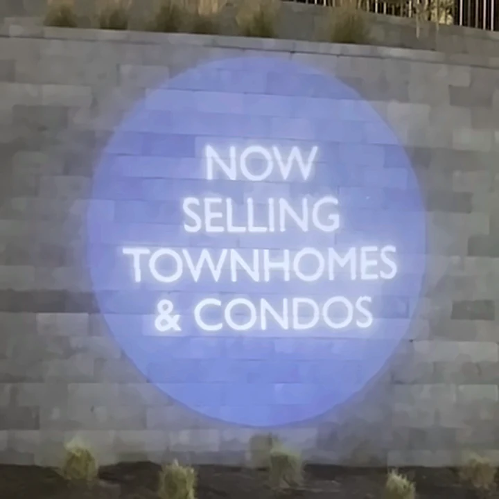 Now Selling Townhomes and Condos projected on The Aire's stone entrance wall at night
