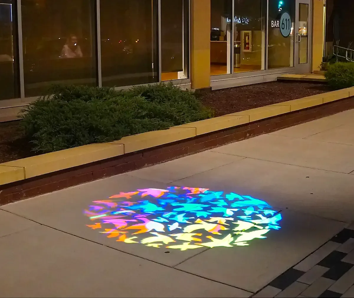 Multicolored bird gobo projected on the sidewalk outside a bar at night — real install