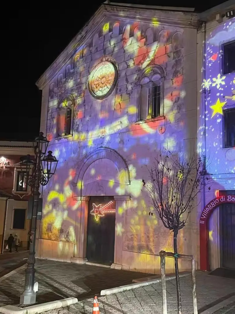 Colorful holiday stars projected across a stone church facade at night
