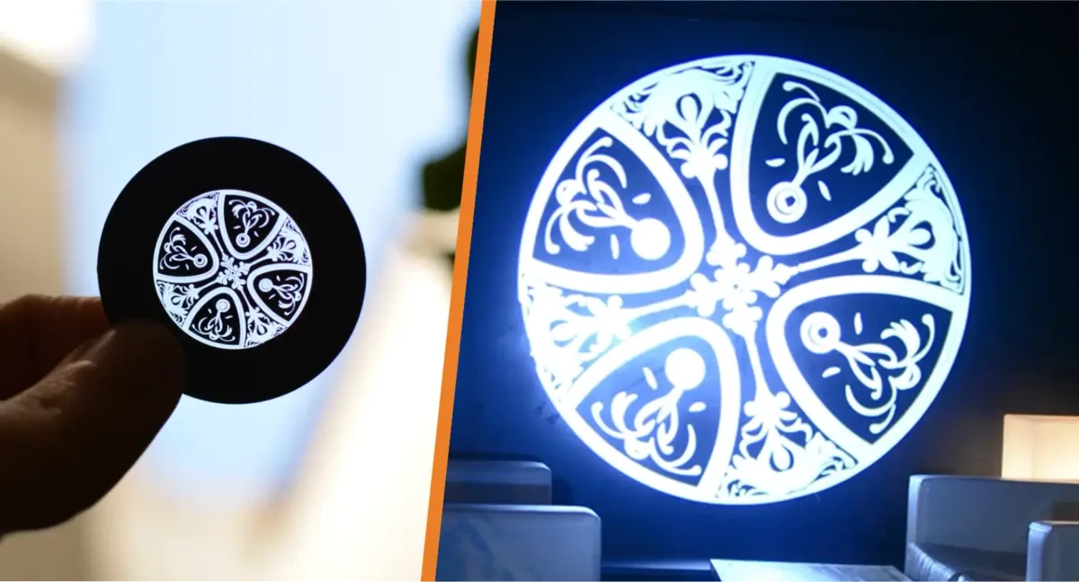 A glass gobo disc held in hand beside its filigree pattern projected on a wall