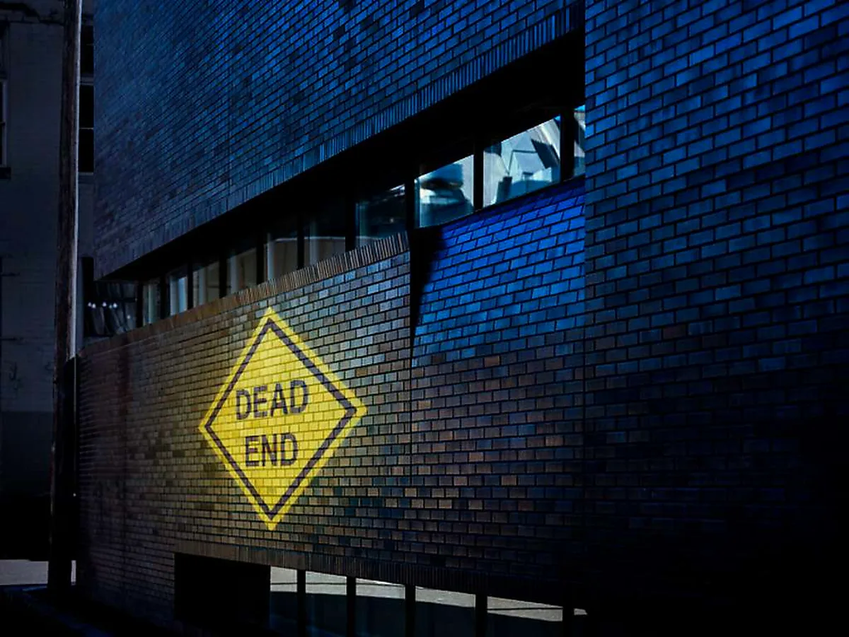 Yellow DEAD END caution sign projected on a dark brick wall in an alley