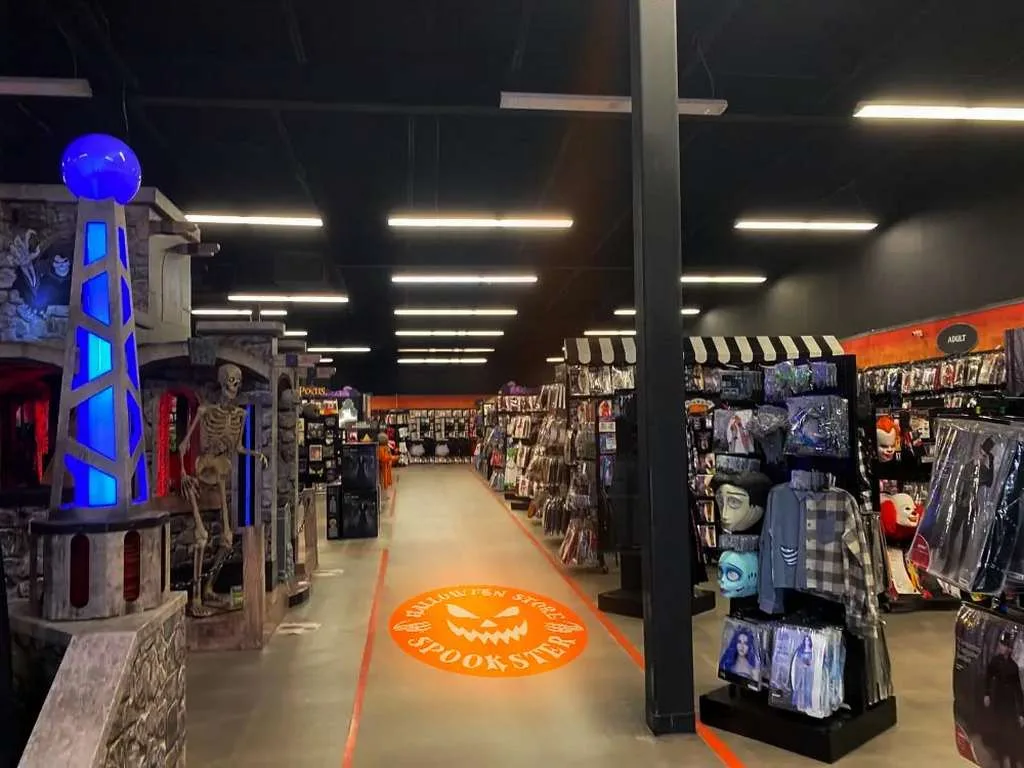 Orange jack-o-lantern SPOOKSTER logo projected on a Halloween store aisle floor