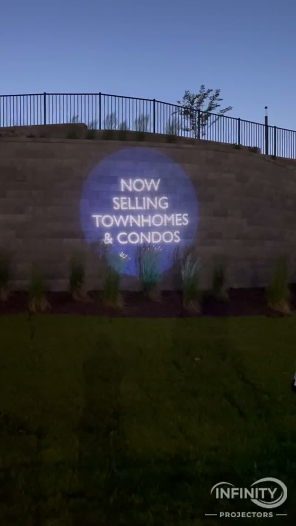 Real-estate logo projected on a large building facade at dusk from a high-wattage projector