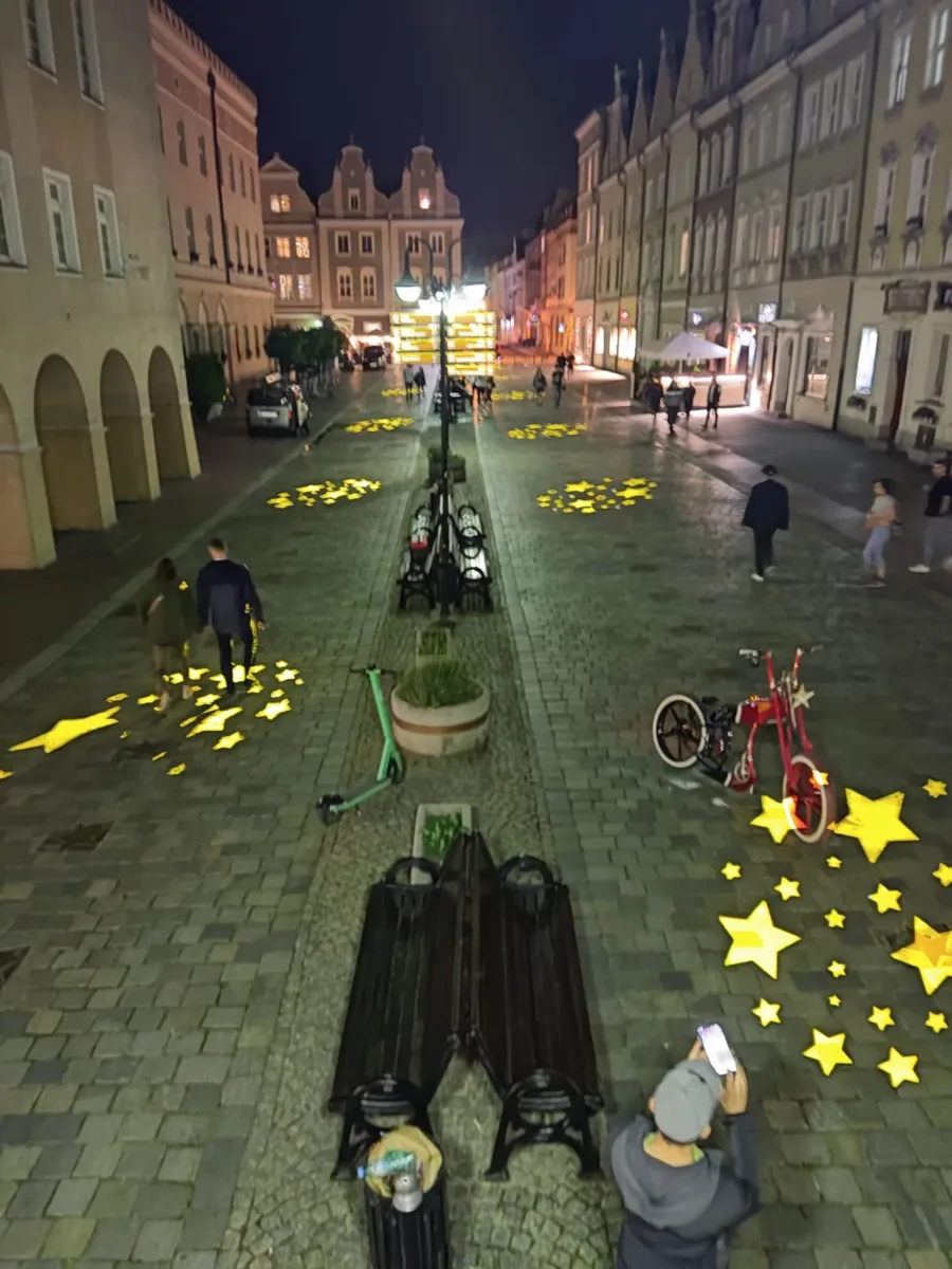 Golden star gobos scattered across an old-town cobblestone square at night