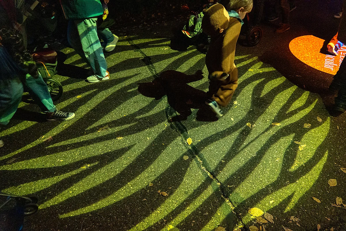 Children in a tiger-stripe light projection along a zoo pathway