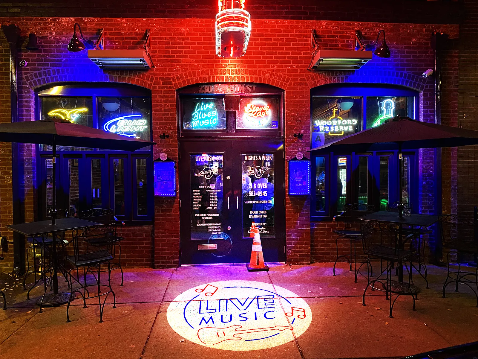 LIVE MUSIC logo projected on the sidewalk outside a brick live-music venue at night
