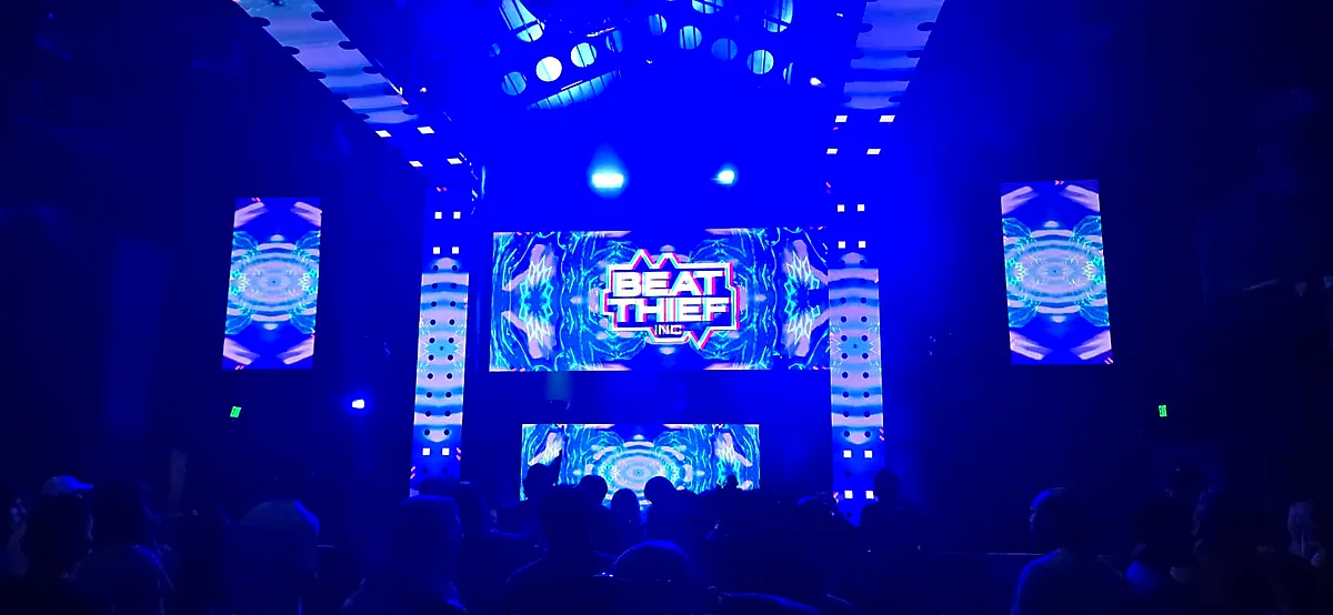 Nightclub DJ booth bathed in blue light with kaleidoscopic LED stage visuals over the crowd