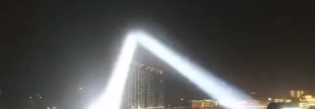 Searchlight beams visible across an entire city skyline at night from a rooftop install