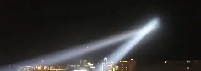 Twin searchlight beams sweeping the night sky in an outdoor install