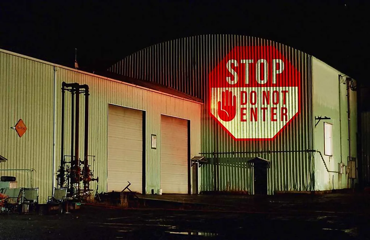 STOP DO NOT ENTER projected large on a corrugated industrial building at night