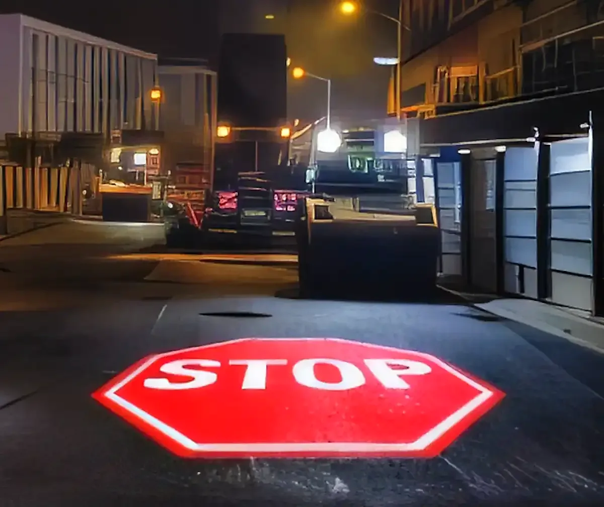 Red STOP octagon beamed onto the asphalt at an industrial yard gate at night