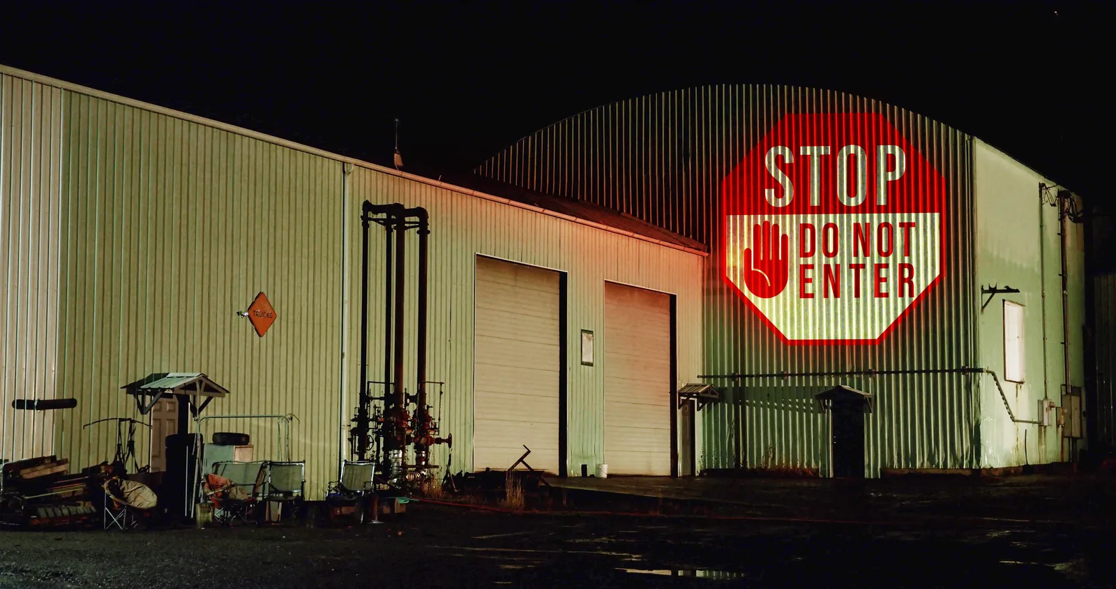 STOP — DO NOT ENTER sign projected on a warehouse exterior wall at night